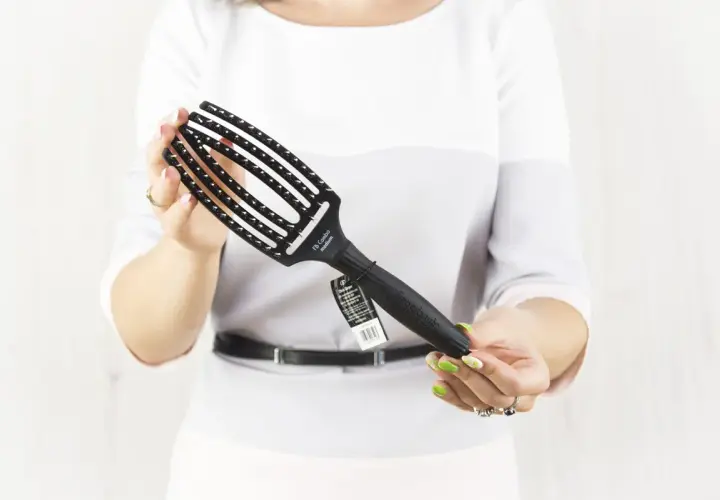 Kobieta trzyma czarną szczotkę do włosów Olivia Garden Fingerbrush.