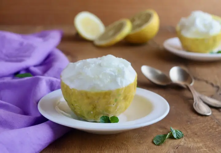 Sorbetto al limone veloce servito in un limone scavato, con limoni affettati e un tovagliolo viola sullo sfondo.