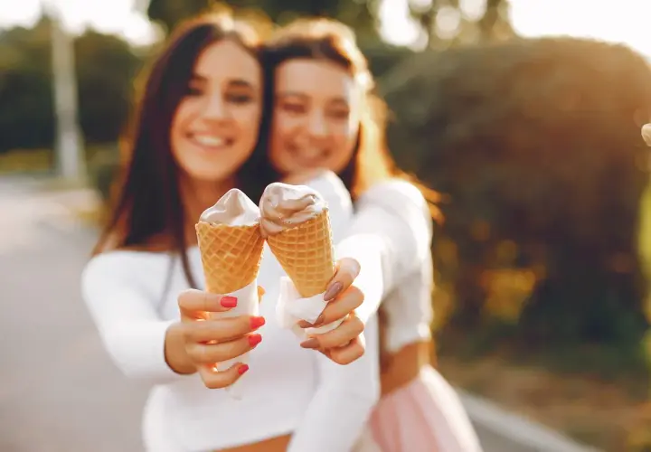 Dwie uśmiechnięte dziewczyny trzymają lody w wafelkach. Czy lody tuczą? Może odrobina przyjemności nie zaszkodzi!