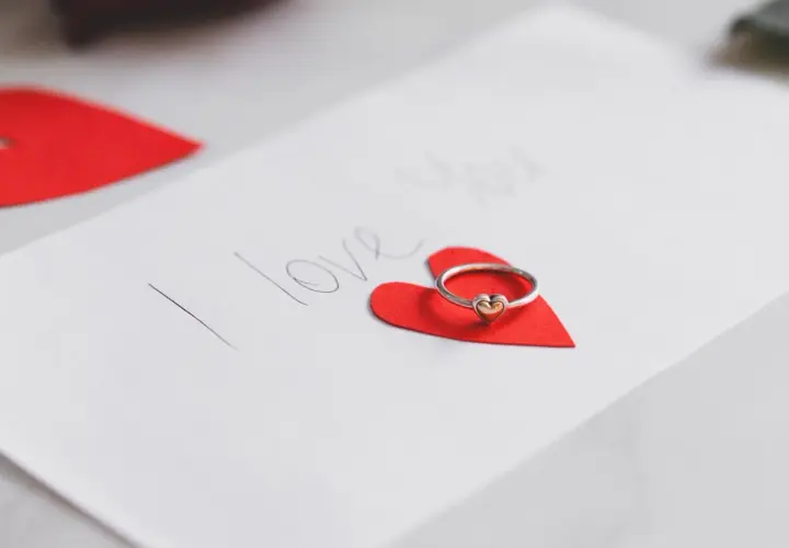 Pierścionek z serduszkiem na czerwonym sercu, obok napis "I love you". Idealne życzenia walentynkowe po angielsku.