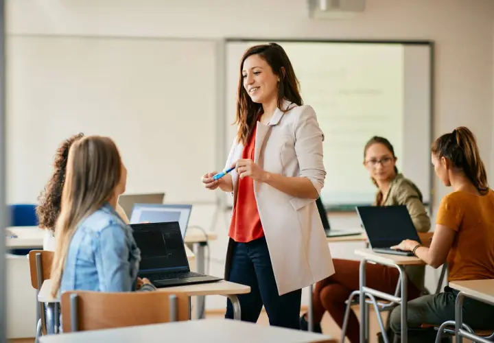 Nauczycielka wyjaśnia studentom, jak zostać nauczycielem zawodu. Uczniowie pracują na laptopach w sali lekcyjnej.