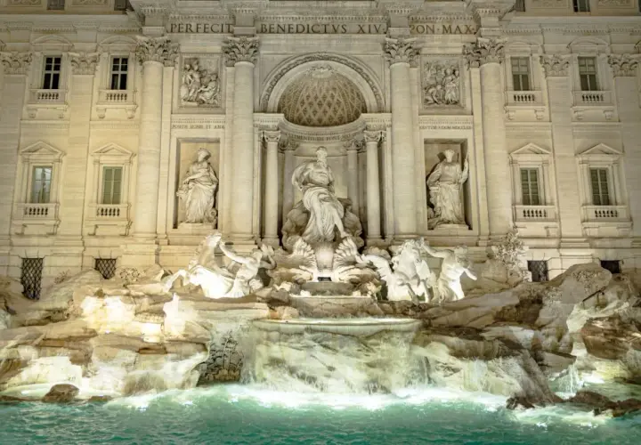 Trevi Fountain at night, with illuminated sculptures and cascading water.