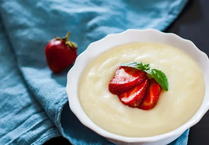 Gładka kaszka manna, czyli semolina co to, podana z truskawkami i miętą na niebieskim tle.