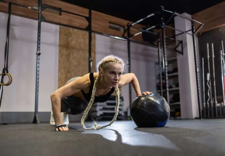 Kobieta w pozie pompki z piłką treningową, idealne ćwiczenie na początek przygody z crossfit.