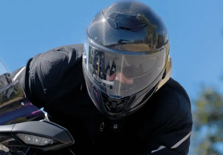 Motociclista con un casco mas silencioso de fibra de carbono, disfrutando del paisaje en un día soleado.