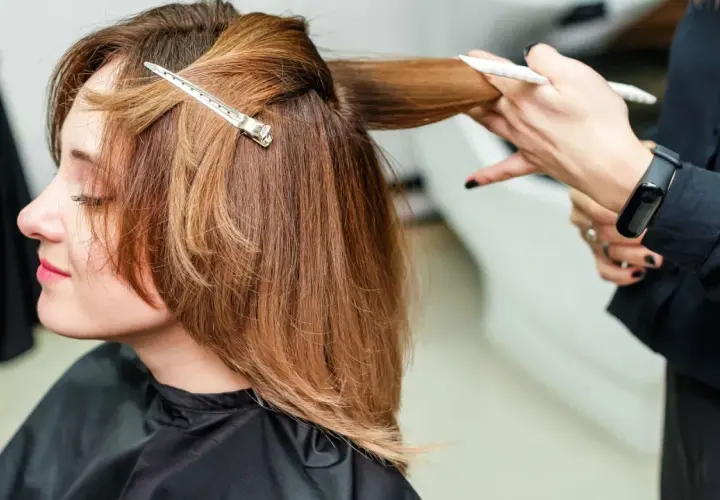 Kobieta z brązowymi włosami do ramion, fryzjerka modeluje pasmo włosów.