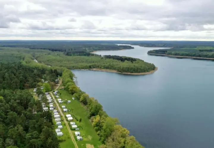 Vue aérienne d'un camping naturiste en Allemagne, bordé par une forêt dense et un lac paisible.