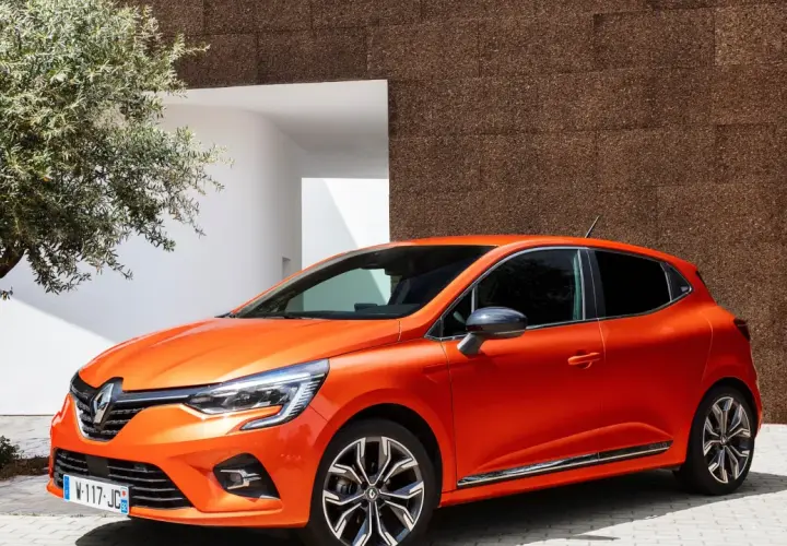 En orange Renault Clio 2026 parkerad vid en modern byggnad med en olivträd i förgrunden.
