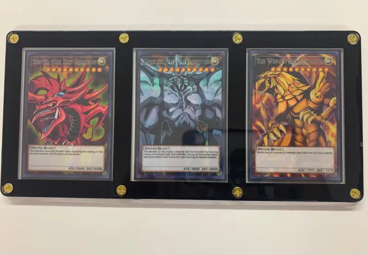 Trzy karty Yu-Gi-Oh! w ramce: Slifer the Sky Dragon, Obelisk the Tormentor i The Winged Dragon of Ra.