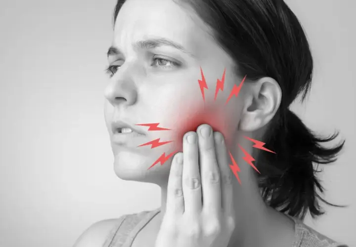 Mujer con dolor de muelas, tocándose la mejilla. Rayos rojos indican el dolor. ¿Qué hacer para el dolor de muelas?