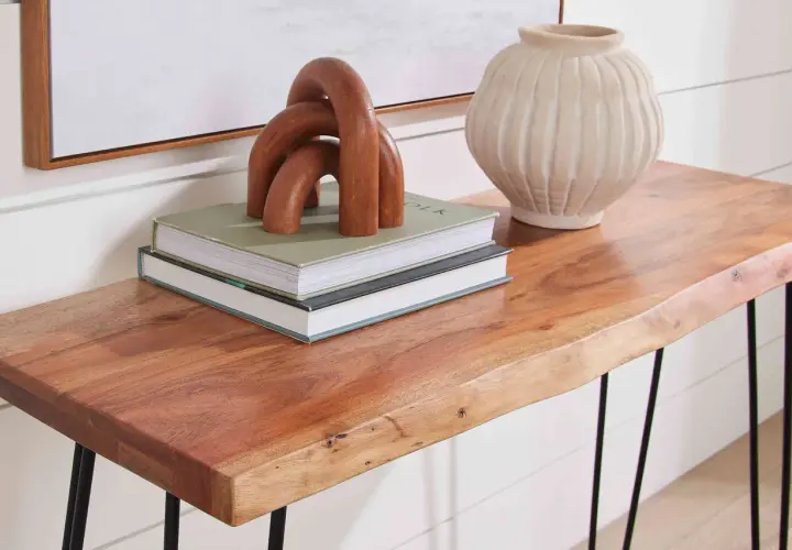 A live-edge acacia hardwood console table displays books, a wooden sculpture, and a textured vase.