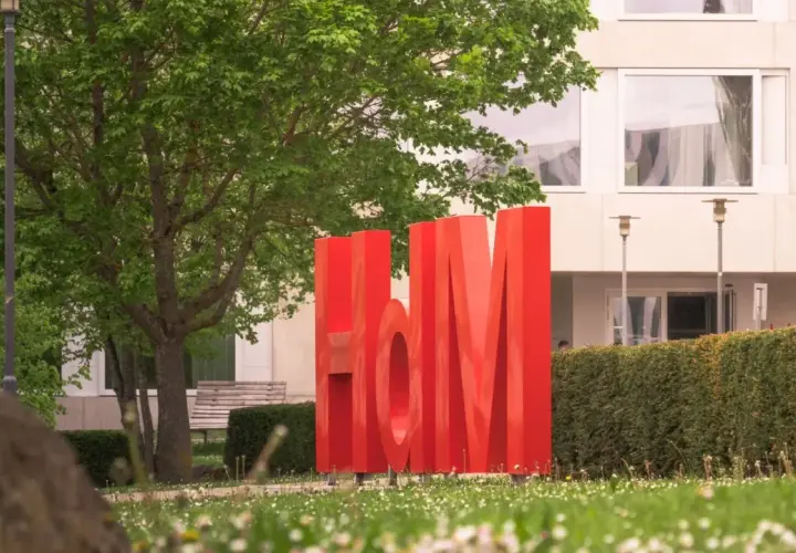Große rote Buchstaben "HdM" vor einem Gebäude. Hier könnte dein berufsbegleitendes Studium in Stuttgart beginnen.