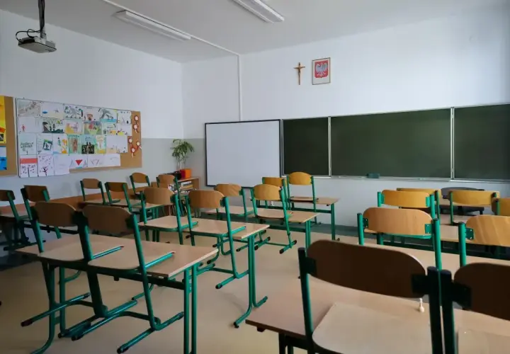 Pusta klasa szkolna z rzędami ławek i krzeseł. Na ścianie tablica, projektor i dziecięce rysunki. Odwołane zajęcia w szkołach sprawiają, że sale wyglądają tak.