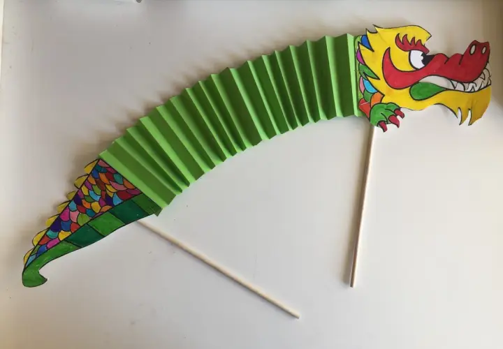 Dragón de papel verde, parte de un manualidades proyecto china infantil. Cabeza colorida y cuerpo en acordeón.
