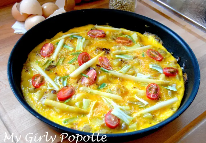 Omelette aux asperges vertes et oignons, garnie de tomates cerises, prête à être dégustée. Une recette simple et savoureuse.