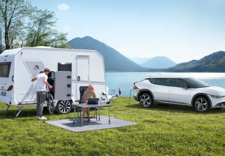 Para wakacyjna z przyczepą kempingową i ładowanym autem elektrycznym nad jeziorem. Idealne na wycieczkę z prawem jazdy B96.