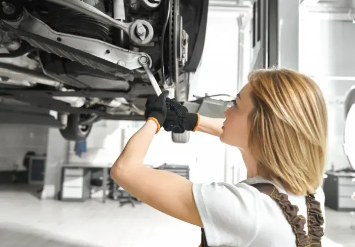 Mechanik pracuje pod samochodem, dokręcając śrubę wahacza. Sprawdź wymiana wahacza cena.