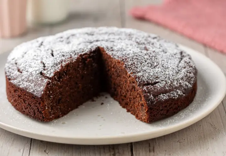 Una fetta è stata tolta da questa torta al cioccolato soffice, cosparsa di zucchero a velo.