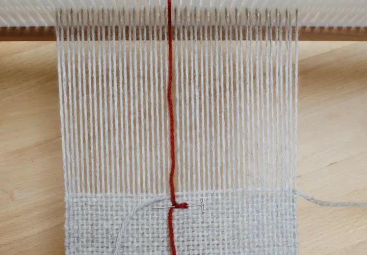 Début d'un tissage sur métier, fils de coton gris et rouge. La technique de tissage se révèle avec chaque passage.