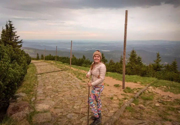 Karpacz-Śnieżka czas wejścia: uśmiechnięta turystka na kamiennym szlaku, w tle rozległa panorama gór.