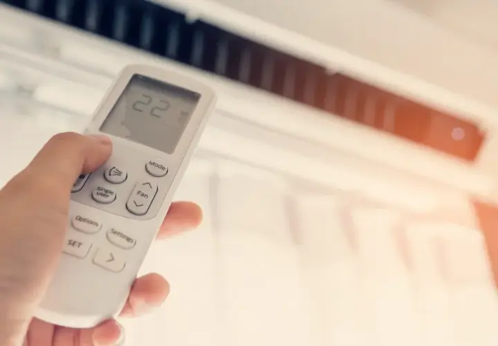 Mano ajustando el control remoto del aire acondicionado, mostrando la temperatura a 22 grados. ¿Qué potencia de aire acondicionado necesito para mi hogar?
