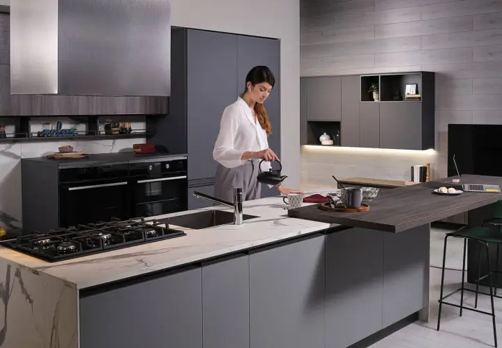 Donna prepara il tè in una moderna isola cucina fai da te con piano in marmo e bancone snack.