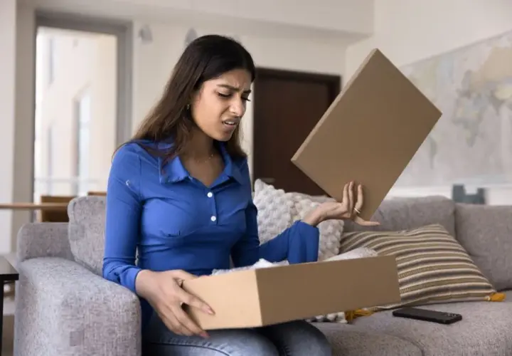 Femme déçue ouvrant un colis, découvrant un produit non conforme à la commande. Elle exprime son mécontentement.