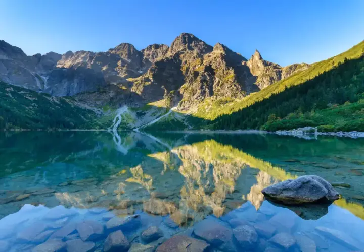 Piękny tatry widok: góry odbijają się w krystalicznie czystej wodzie jeziora, otoczonego zielonymi lasami.