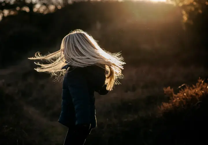 Dziecko z rozwianymi blond włosami w świetle zachodzącego słońca.