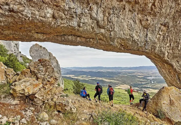 Senderistas disfrutan de vistas panorámicas en rutas por Navarra, bajo un arco natural de roca.