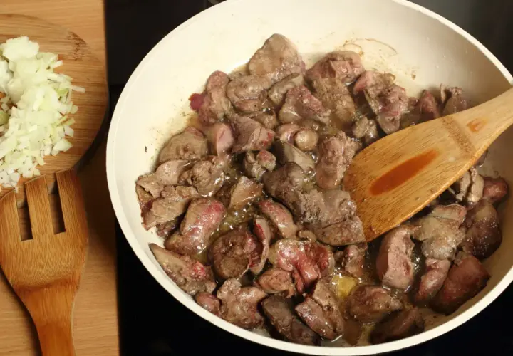 Smażona wątróbka na patelni, obok posiekana cebula. Czy pies może jeść wątróbkę? Tak, ale z umiarem.