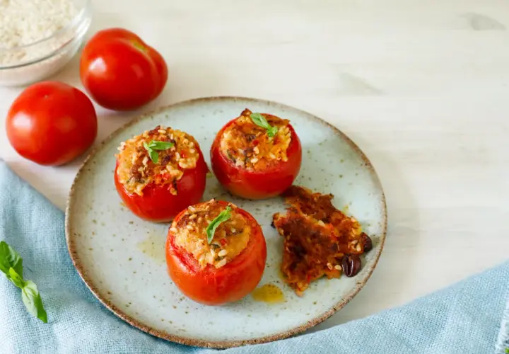 Pomodori ripieni tonno e riso, guarniti con basilico, su un piatto con un contorno croccante.