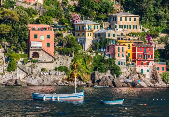 Des maisons colorées s'accrochent à la falaise sur la **riviera italienne où aller**. Des bateaux flottent paisiblement dans l'eau bleue.