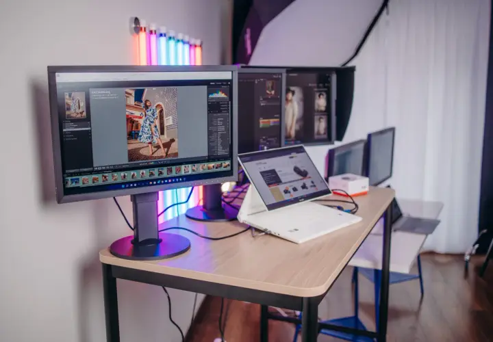 Profesjonalny monitor do obróbki zdjęć, z programem Lightroom, pokazuje zdjęcie kobiety w sukience. Obok laptop i inne monitory.
