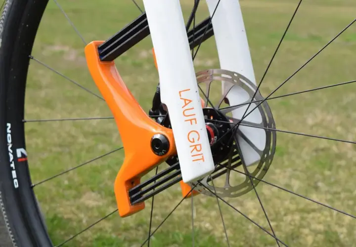 Close-up of a bright orange and white Lauf Grit fork on a bicycle wheel, ready for adventure.