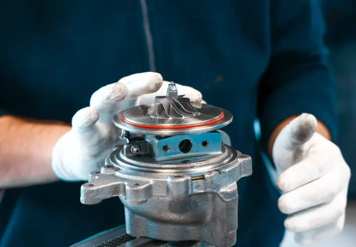 Ręce w białych rękawiczkach trzymają turbosprężarkę, gotową do montażu. To serce potężnego silnika twin turbo.