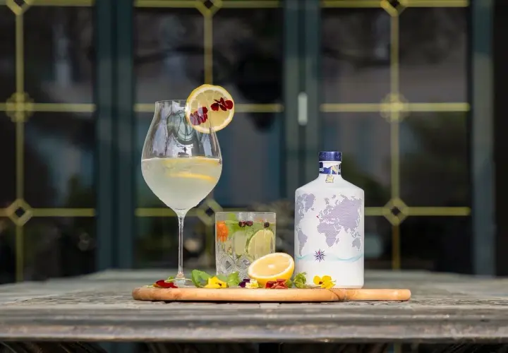 Jak przygotować infuzowany alkohol, np. wódkę o smaku chilli? Na stole stoją drinki, cytryny, zioła i butelka z mapą świata.