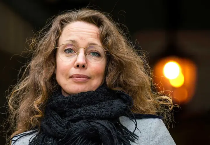 Sara Gordan dotter med sitt långa, lockiga hår och en svart halsduk. Hon bär glasögon och tittar rakt in i kameran.