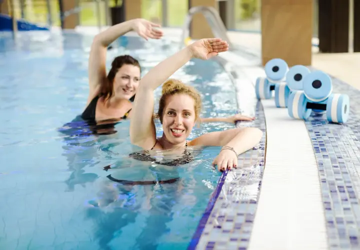 Dwie kobiety ćwiczą w basenie. Obok leżą hantle do aquafitness. Sprawdź nasz primavera basen cennik!