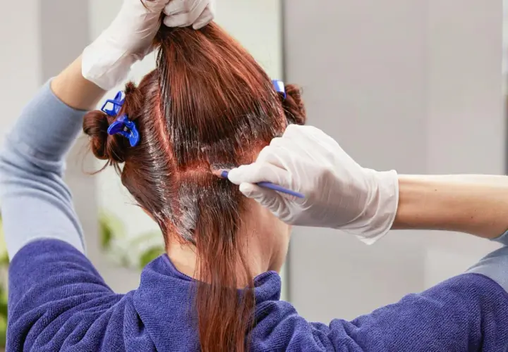 Persona se tiñe el pelo en casa, aplicando tinte con un pincel.