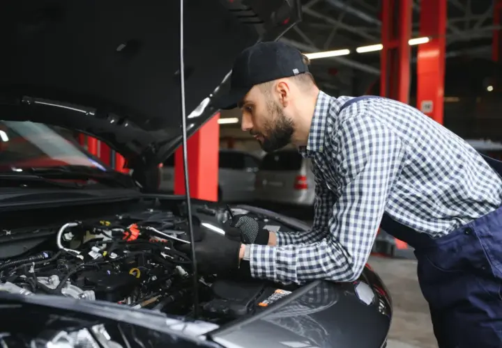 Mechanik w czapce i kratowanej koszuli bada silnik samochodu. Wygląda na to, że próbuje rozwiązać problem, który mógł wpędzić auto w **tryb awaryjny**.