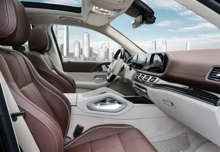 Wnętrze luksusowego **Mercedes GLS 2025** z brązową skórzaną tapicerką i nowoczesnym panelem. Widok na miasto przez panoramiczny dach.