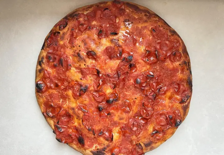 Focaccia rossa con pomodorini succosi e crosta dorata, un'esplosione di sapore mediterraneo.
