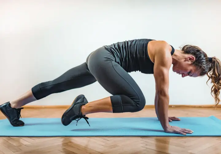 Kobieta wykonuje ćwiczenie w stylu hiit, co to za trening? Dynamiczne ruchy na macie, budowanie siły i wytrzymałości.