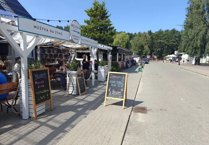 Dębki promenada: lokal Belona zaprasza na muzykę na żywo i koncerty. W tle widać letnie ogródki i spacerujących ludzi.