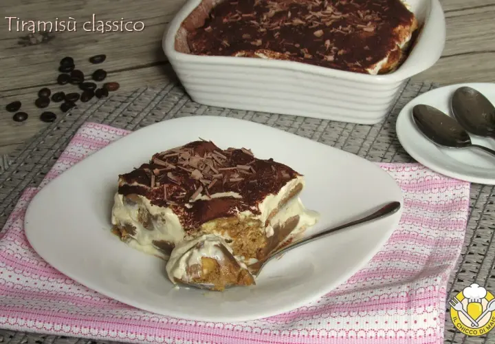 Una fetta di tiramisù classico, con savoiardi inzuppati nel caffè e crema al mascarpone, spolverato di cacao e scaglie di cioccolato. La ricetta del tiramisù è un classico intramontabile.