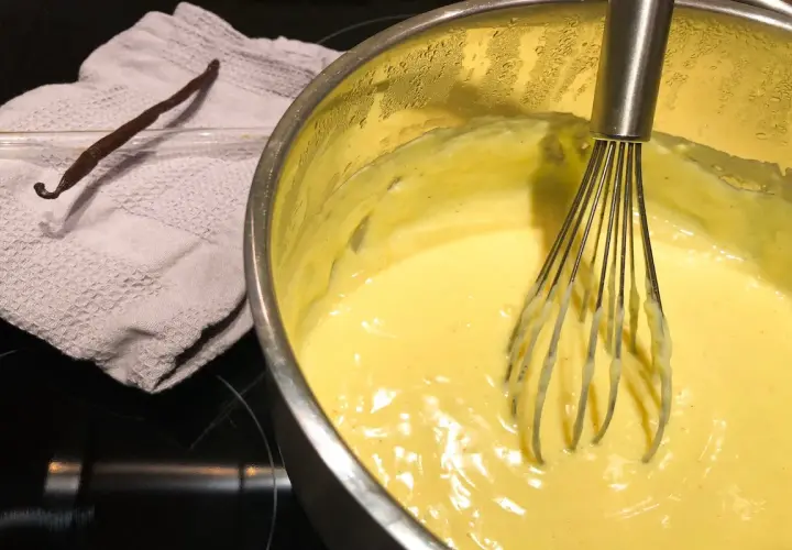 Crema pasticcera senza latte in preparazione, con bacca di vaniglia e frusta.