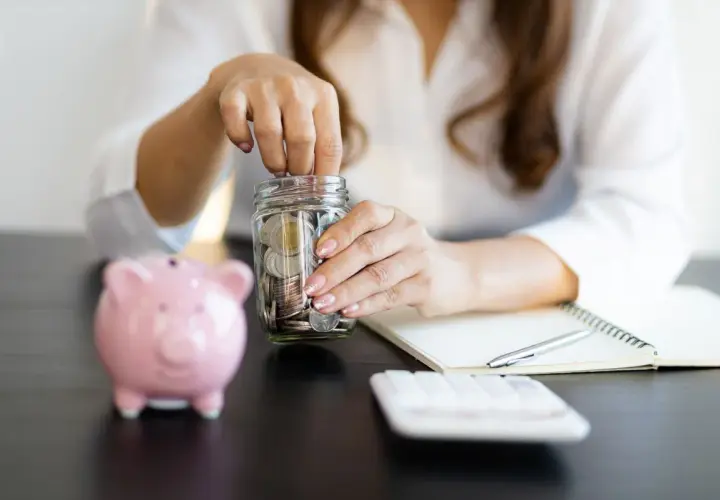 Kobieta wkłada monety do słoika, budując oszczędności. Czy to wystarczy, by osiągnąć cel: ile oszczędności w wieku 30 lat?