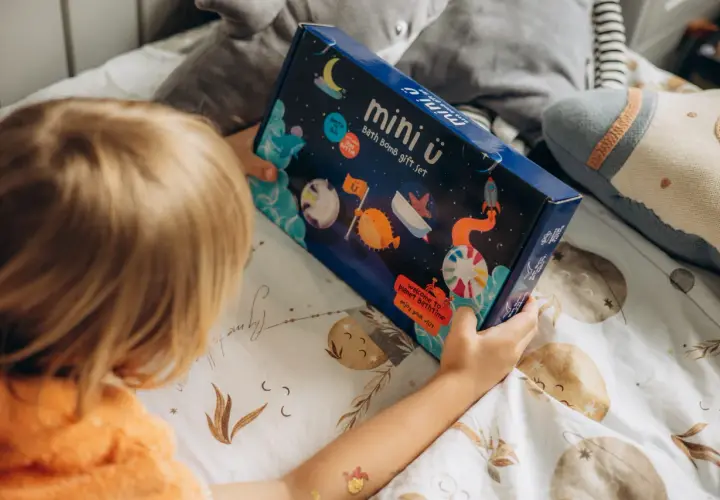Dziecko trzyma pudełko z zestawem do kąpieli "mini ü". Na opakowaniu są kosmiczne motywy, które podpowiadają, jak używać kuli do kąpieli dla wspaniałej zabawy.
