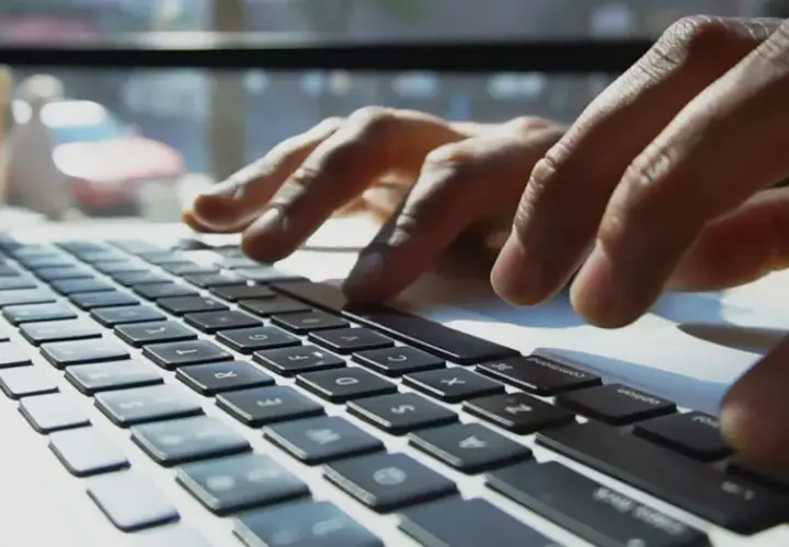 Mains sur un clavier d'ordinateur portable, une tasse de café à proximité. L'utilisateur interagit avec un chatbot helpdesk pour obtenir de l'aide.